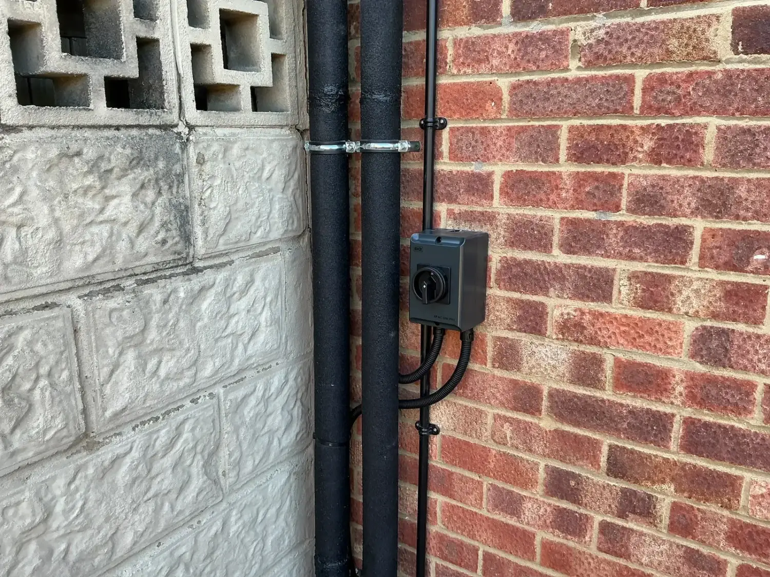 Anthracite BG rotary isolator beside the insulated heat pump pipework on the outside wall